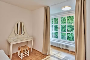 A room with a white vanity, a mirror, a stool, a window with a view of greenery, and a radiator. - Altstadt Apartments Melk - Gartenapartment mit Terrasse Top 4 - Altstadt Apartments Melk (Melk)