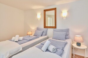 Ein Hotelzimmer mit zwei Betten, gestreifter Bettw äsche, einem Spiegel, Wandleuchten und einem Nachttisch mit Lampe.