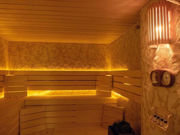 Sauna, jossa on puiset penkit, seinälle kiinnitetty kello ja hylly, jossa on pulloja.