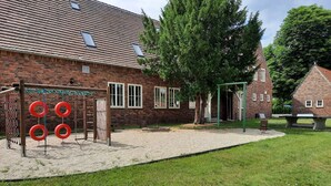 A playground with swings and climbing structures, a brick building with windows, and a grassy area. - Zimmer 5 - Seenland-oase Reppist (Senftenberg)