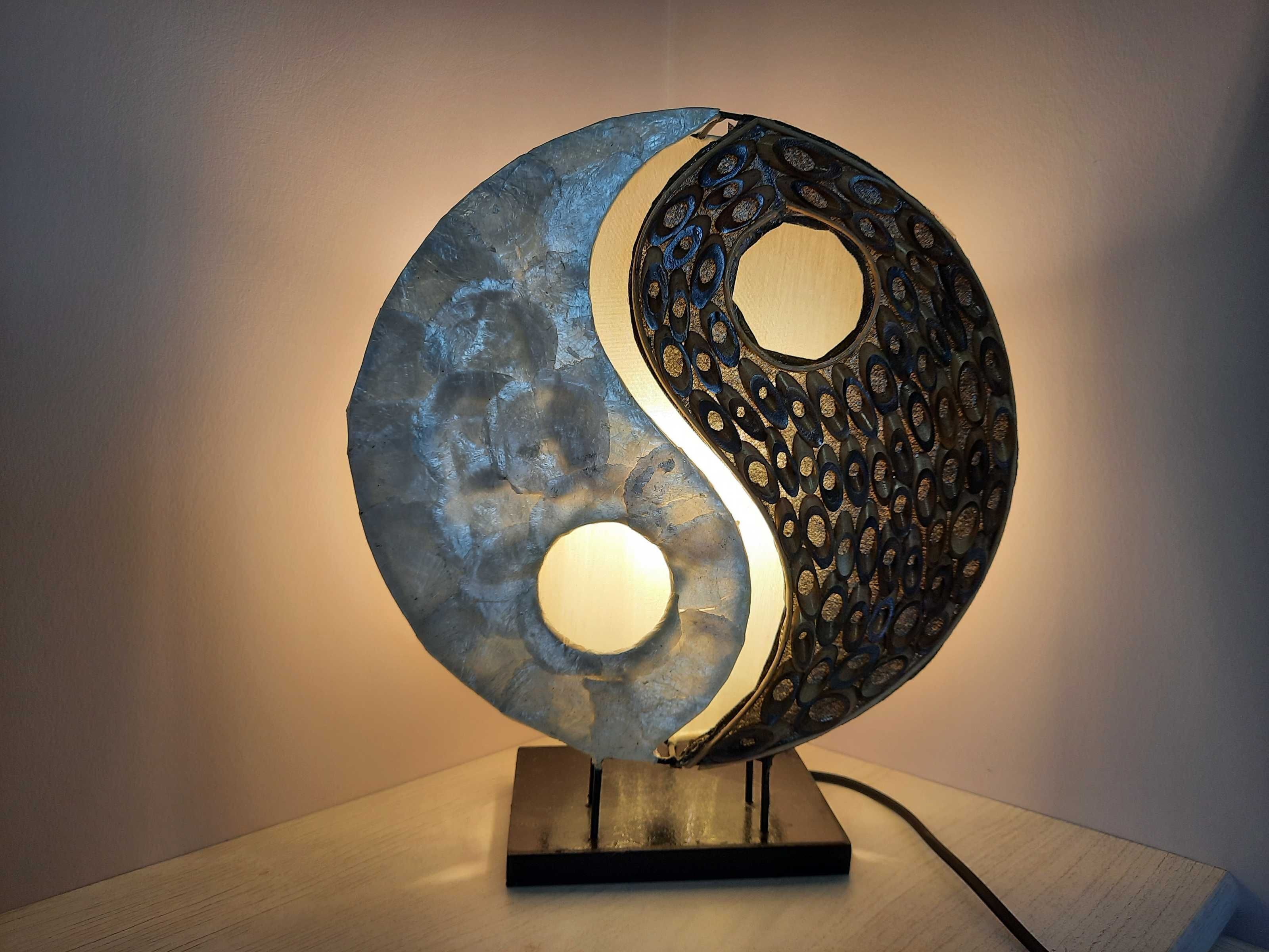Una scultura sferica con simbolo dello yin e yang, caratterizzata da una superficie strutturata e una fonte di luce centrale.