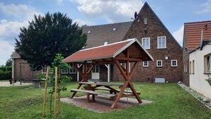 Een picknickplaats met een houten tafel en banken, omgeven door een gebouw met bakstenen muren en een schuin dak.