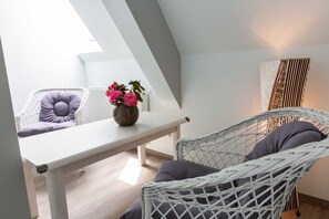 A modern loft bedroom with a sloped ceiling, a white wicker chair, a white bench, and a vase with flowers.