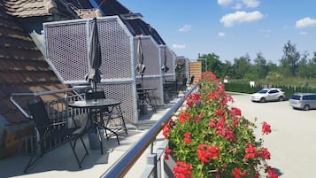 Ein Balkon mit Sitzgelegenheit, einem Metallgeländer und einer Reihe roter Blüten.