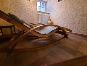Un fauteuil à bascule en bois, dans une pièce aux murs de pierre et dotée d’un radiateur.