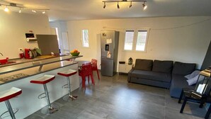 Una cocina moderna con una isla central, taburetes rojos, un sofá gris y un área de comedor.