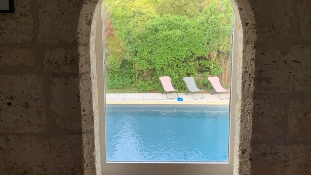 Et buet vindue med udsigt til en swimmingpool og liggestole.