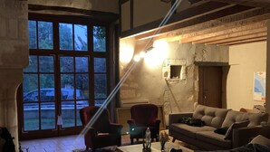 En hyggelig stue med pejs, store vinduer og en blanding af moderne og rustik møblering.