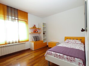 Ein Schlafzimmer mit Holzboden, einem Bett mit Blumenmuster-Überwurf, einem Nachttisch, einer Kommode und einem Fenster mit Vorhängen.