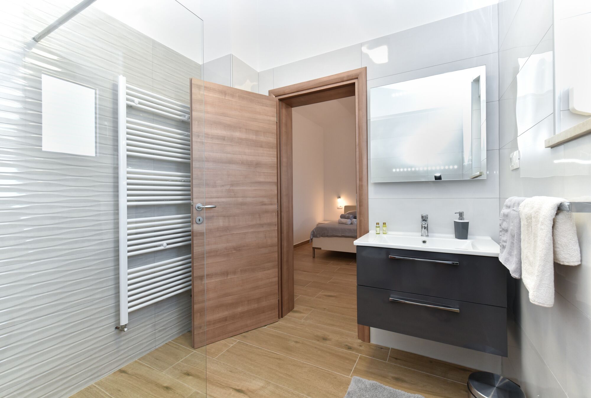 A modern bathroom with a wooden door, a mirror, a sink, and a towel rack.