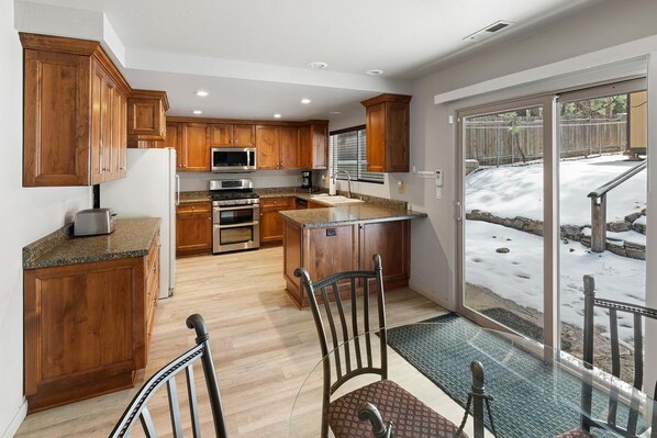 A kitchen with wooden cabinets, a central island, and a view of a snowy outdoor area through a glass door.