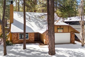 Une maison à deux étages avec un garage, entourée d’arbres et recouverte de neige.