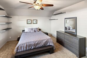 Une chambre à coucher comprenant un lit, une commode, un ventilateur de plafond et des étagères fixées au mur.