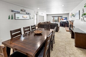 A dining area with a wooden table and chairs, a sofa, and a television in the background.
