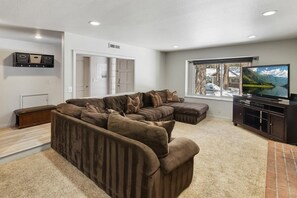 A living room with a sectional sofa, a flat-screen TV, and a window with a view of a lake. - Laurel Lodge by Destination Big Bear : Close to Snow Summit and Short Drive to Village & Lake! Fenced Yard! (Big Bear Lake)