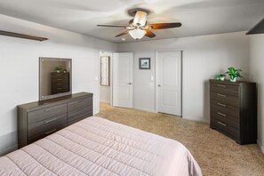 Une chambre à coucher comprenant un lit, une commode, une armoire, un ventilateur de plafond et une porte donnant sur une autre pièce.