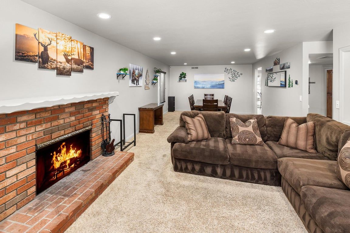 A living room with a brick fireplace, a brown sectional sofa, and a dining area with a table and chairs.
