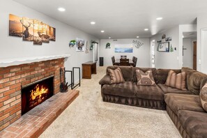 A living room with a brick fireplace, a brown sectional sofa, and a dining area with a table and chairs.