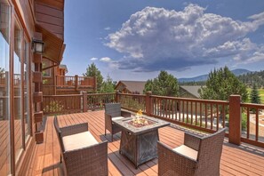 A wooden deck with outdoor furniture and a fire pit, overlooking a mountainous landscape.
