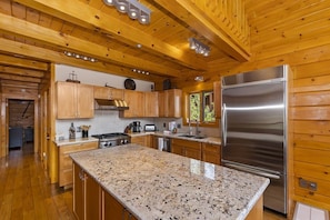 A kitchen with wooden cabinets, a granite countertop, stainless steel appliances, and a window providing natural light. - Luxury Log Home with Mountain Views! Quiet Family Neighborhood! Gameroom! Firepit! (Big Bear City)