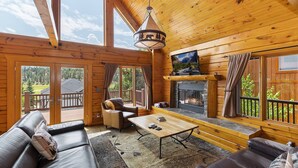 Interior acogedor de una cabaña con chimenea, paredes de madera y ventanas amplias que ofrecen vistas panorámicas.