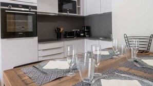 Una cocina moderna con armarios blancos, horno empotrado, microondas y cafetera. Hay una mesa de comedor con individuales y vasos.