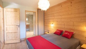 Un dormitorio con pared de madera, una cama con almohadas rojas, una araña y una puerta de madera.