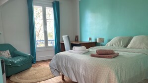 Ein Schlafzimmer mit Bett, Sessel, Schreibtisch und einem Fenster mit Vorhängen.