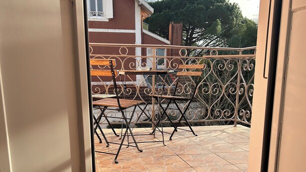 Ein Zimmer mit Holzboden, einer Schiebetür zu einer Terrasse im Freien, die eine Metallreling und zwei Holzstühle hat.