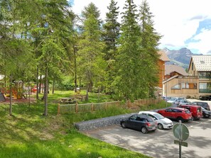 A parking area with cars, a playground, and a building with a mountain view.