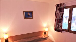 Un dormitorio con cama, dos lámparas de noche, un cuadro en la pared y una ventana con cortinas.