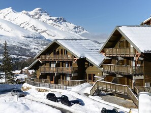 A chalet-style hotel with wooden balconies, set against a snowy mountain backdrop.