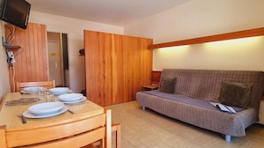 A compact living space with a dining table set for four, a sofa, and a television mounted on the wall. - Cozy studio with snow front view, close to chairlift and shops (Le Dévoluy)