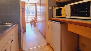 A compact kitchen with a microwave, a small refrigerator, and wooden cabinets. - Cozy studio with snow front view, close to chairlift and shops (Le Dévoluy)