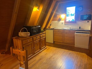 A cozy kitchen with wooden cabinets, a microwave, a dishwasher, and a window with a view of greenery. - 3-Room Chalet with Terrace and Free Parking (La Joue du Loup)