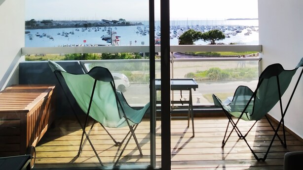 A balcony with a view of a marina, a wooden table, two green folding chairs, and a yellow and white striped awning. - Studio Face mer et Proche Marché Pornichet (Pornichet)