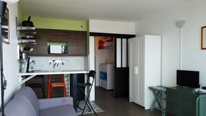 A compact living space with a kitchenette, a grey sofa, a TV, and a small dining area. - Studio Face mer et Proche Marché Pornichet (Pornichet)