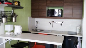 A compact kitchen with a white countertop, a sink, and a microwave. There are two chairs, one red and one black, and a small shelf with kitchen utensils. - Studio Face mer et Proche Marché Pornichet (Pornichet)