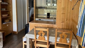 Una cocina compacta con armarios de madera, una mesa de comedor con sillas y un pequeño cubo de basura.