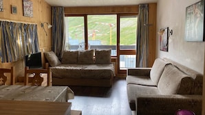 Un salón acogedor con un conjunto de sofás, una mesa de madera y vistas a un paisaje verde a través de grandes ventanales.