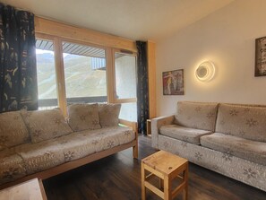 Une pièce comprenant deux canapés, une table basse en bois et une grande fenêtre donnant sur un paysage montagneux.