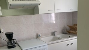 A kitchen with a washing machine, an oven, a coffee maker, and a sink. - Small house in village center with large garden, 7km from beaches.   (Lit-et-Mixe)