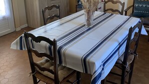 A dining area with a long table, chairs, and a vase with dried flowers. - Small house in village center with large garden, 7km from beaches.   (Lit-et-Mixe)