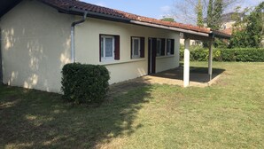 A single-story building with a tiled roof, a covered porch, and a small garden area. - Small house in village center with large garden, 7km from beaches.   (Lit-et-Mixe)