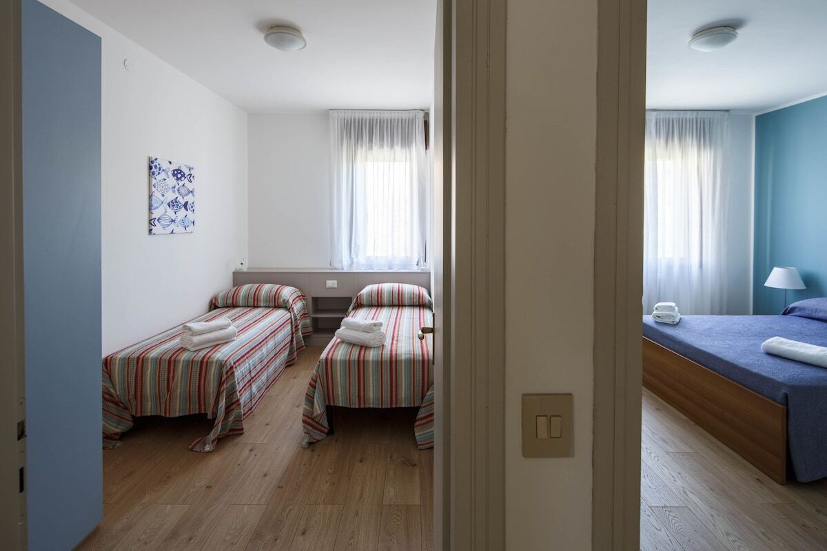 A hotel room with two single beds, a small table, a lamp, and a window with curtains.