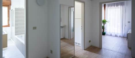A spacious room with a large mirror, wooden flooring, and a view of a bathroom with a bathtub.