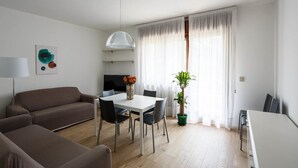 A modern living room with a sofa, dining table, chairs, a TV, and a plant.
