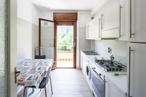 Uma cozinha compacta com fogão a gás, máquina de lavar roupa e um espaço de refeições com mesa e cadeiras.