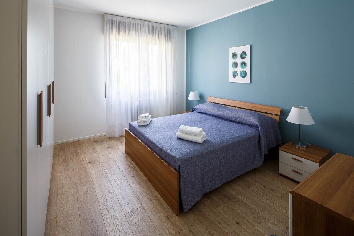 Una camera da letto con un letto, comodini, una lampada, una finestra con tende e un quadro appeso al muro.