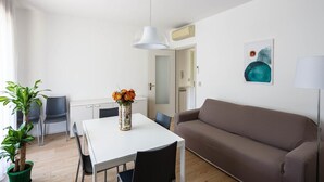 A modern living room with a white dining table, a brown sofa, and a single potted plant.